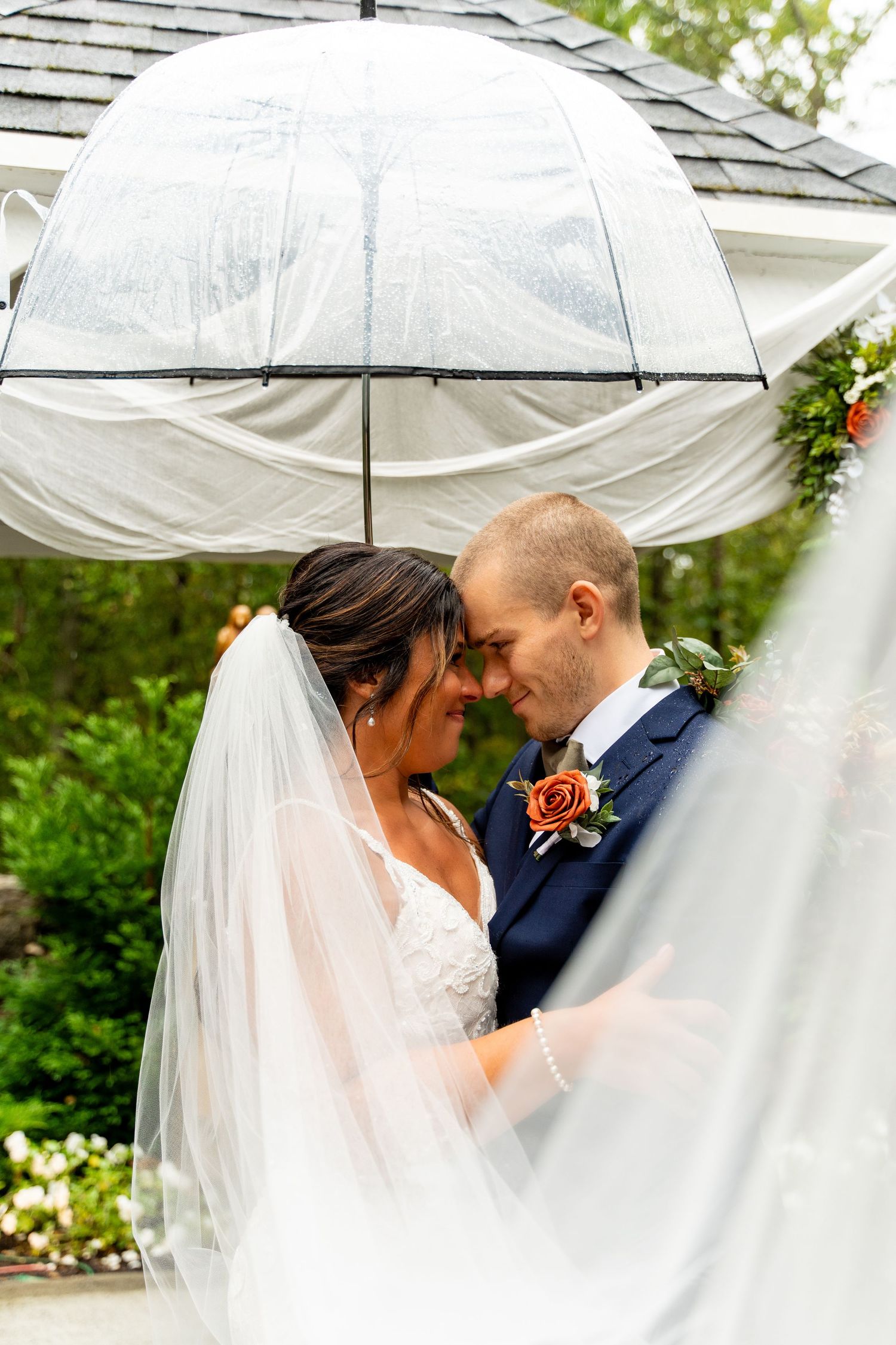 Intimate moment shared under clear umbrella during outdoor wedding ceremony.