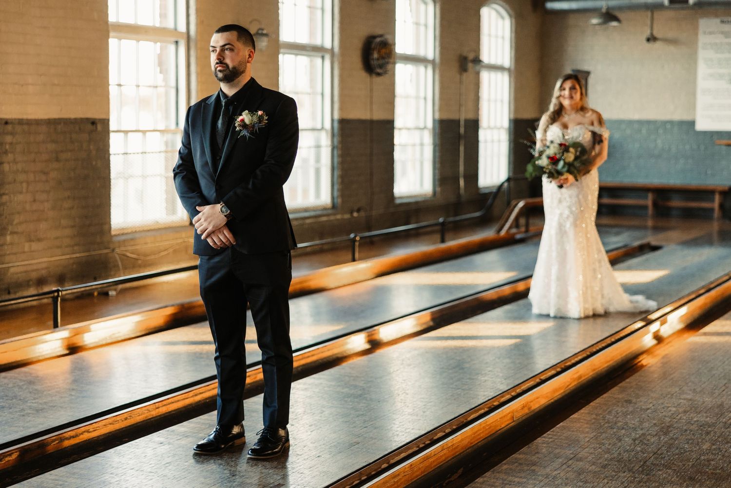 Bride and groom standing apart on bowling lanes in industrial venue.