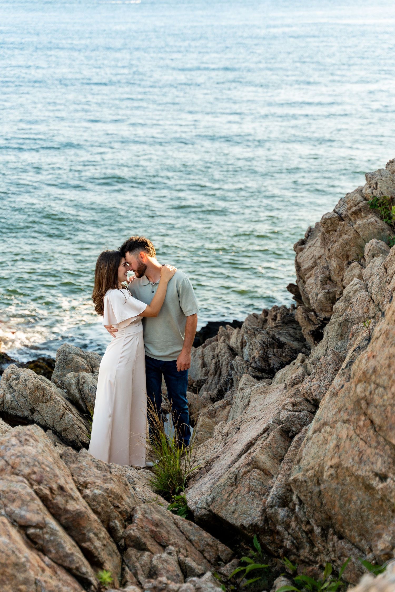 Romantic couple embracing on rocky coastal cliffs overlooking the ocean at sunset.