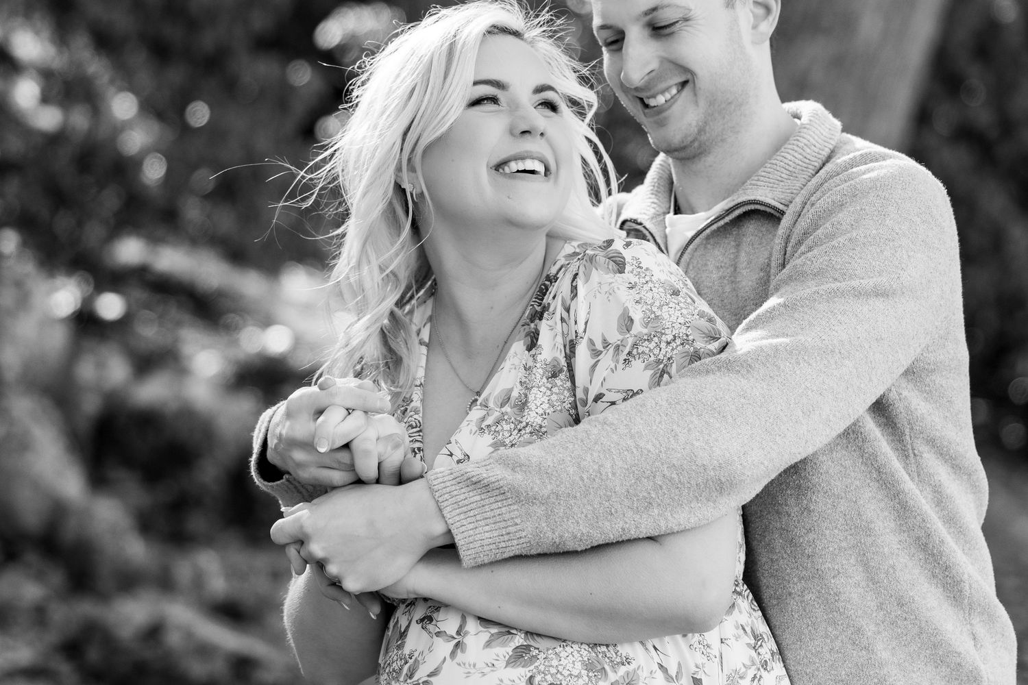 A couple shares a joyful embrace outdoors in black and white.