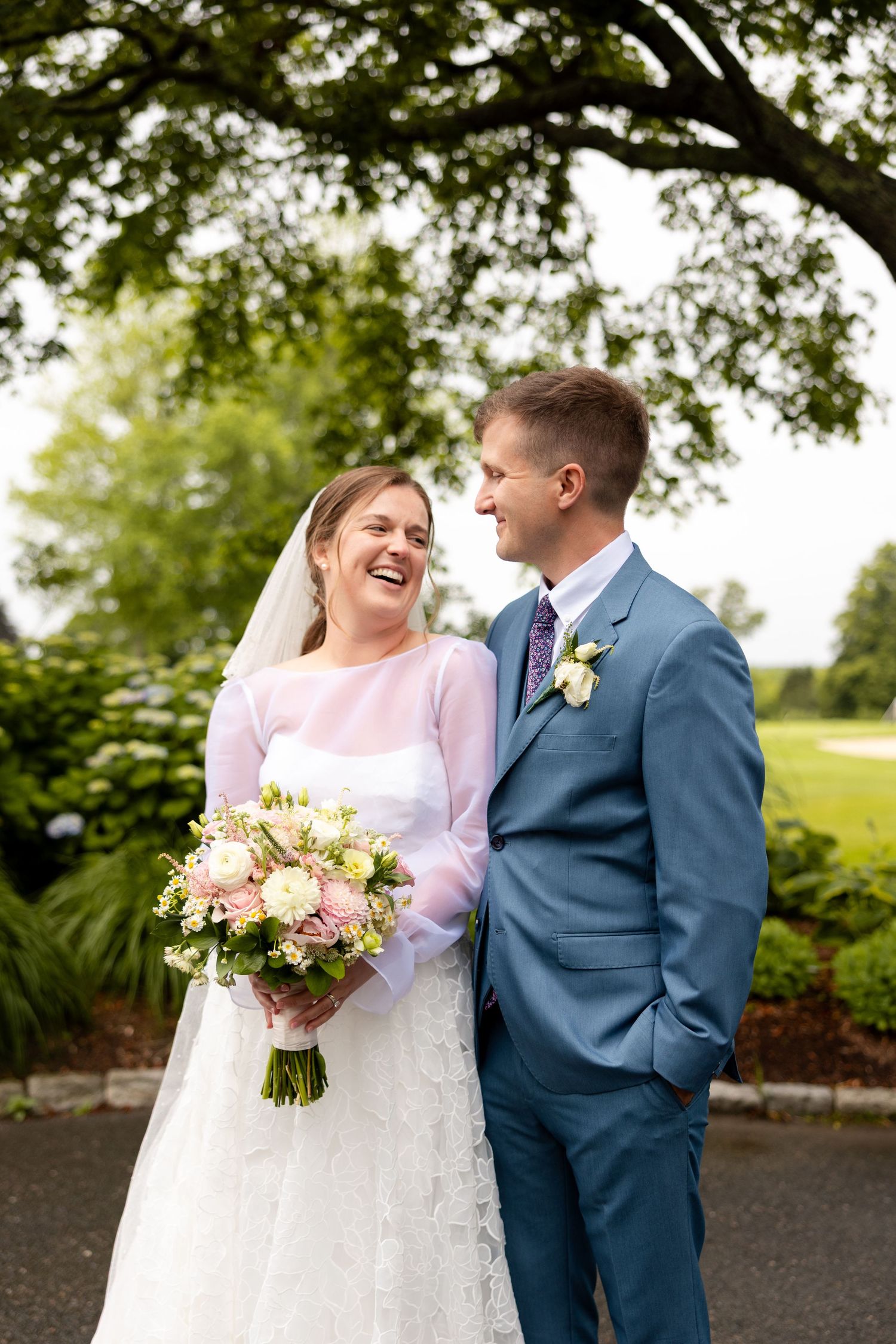 Joyful wedding couple shares tender moments in an outdoor garden setting wearing blue suit and white gown.