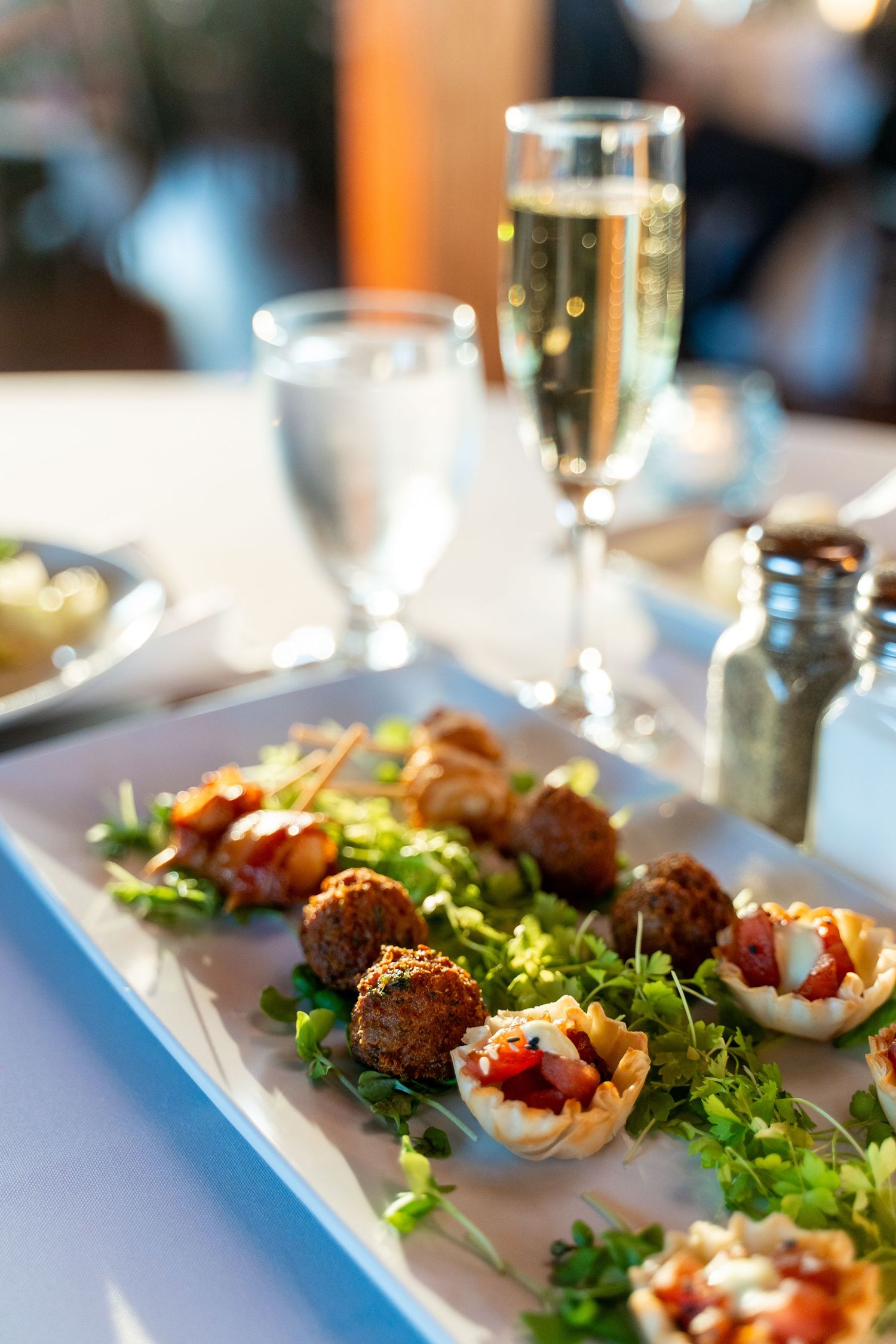 Appetizer plate with hors d'oeuvres and champagne flute on white tablecloth.