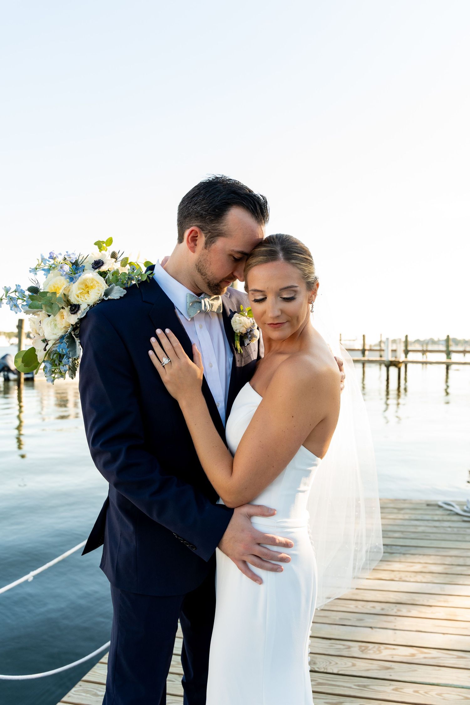 Romantic moment between newlyweds on dock with water in background.