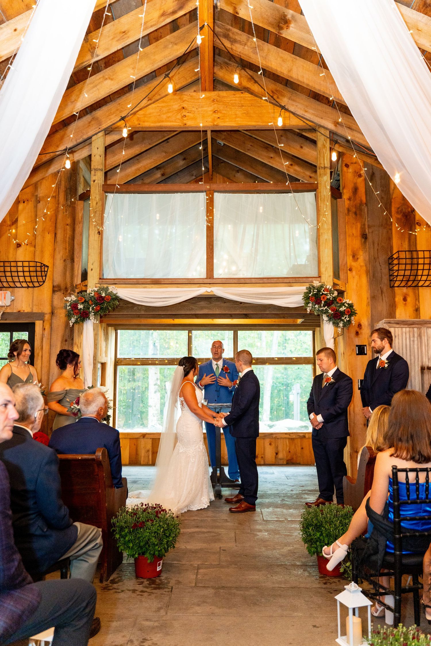 Indoor barn wedding ceremony with exposed wooden beams and white fabric draping.