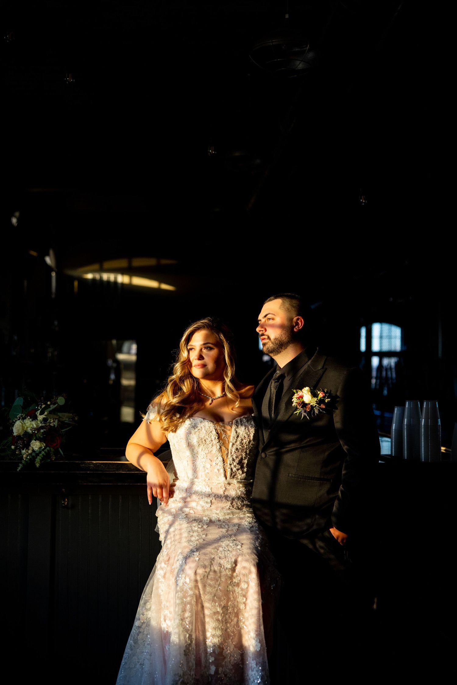 Dramatic nighttime portrait of newlyweds illuminated by golden light in dark indoor space.