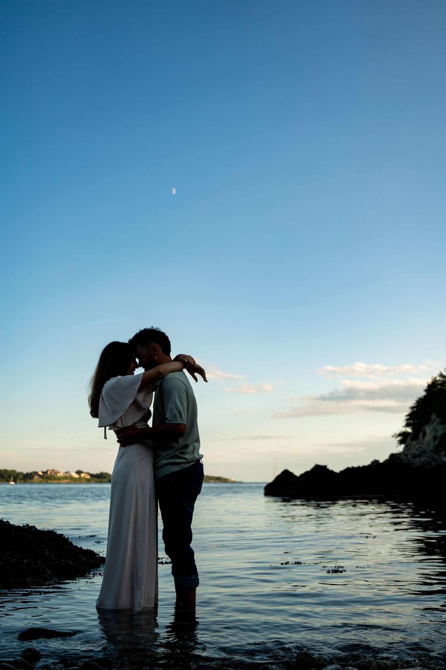 Silhouetted couple sharing intimate moment at water's edge during sunset.