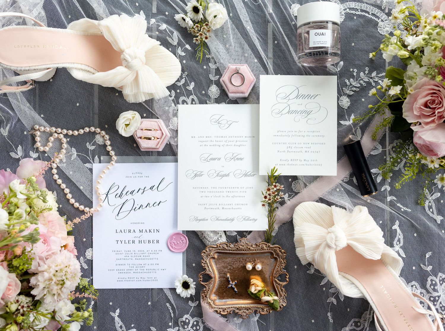 Elegant wedding invitation suite with pink florals and calligraphy displayed on dark marble with candles and pearls.
