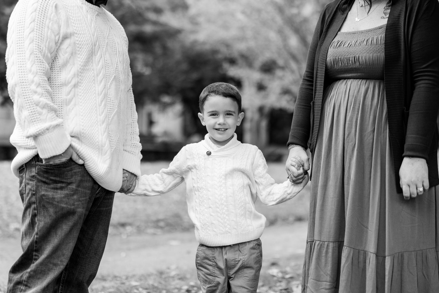 Black and white portrait of child holding hands with parents outdoors.