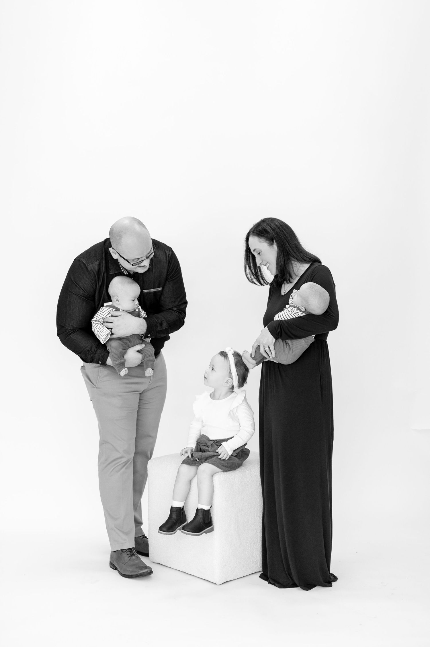 Black and white portrait of family with toddlers in minimalist studio setting.