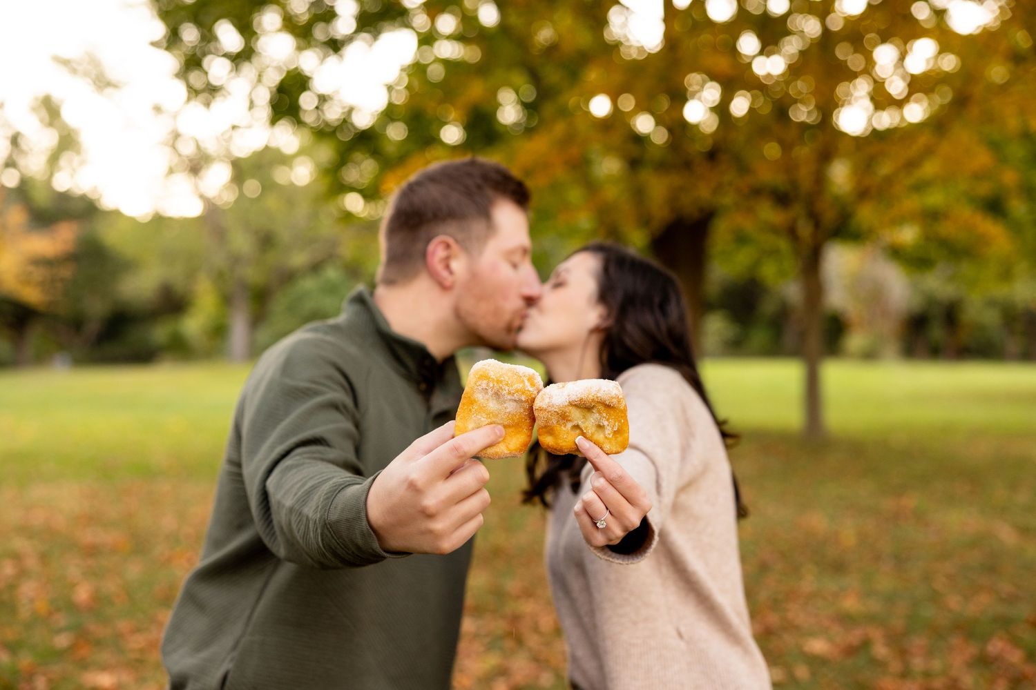 A couple sharing croissants and laughing together in an autumn park setting.