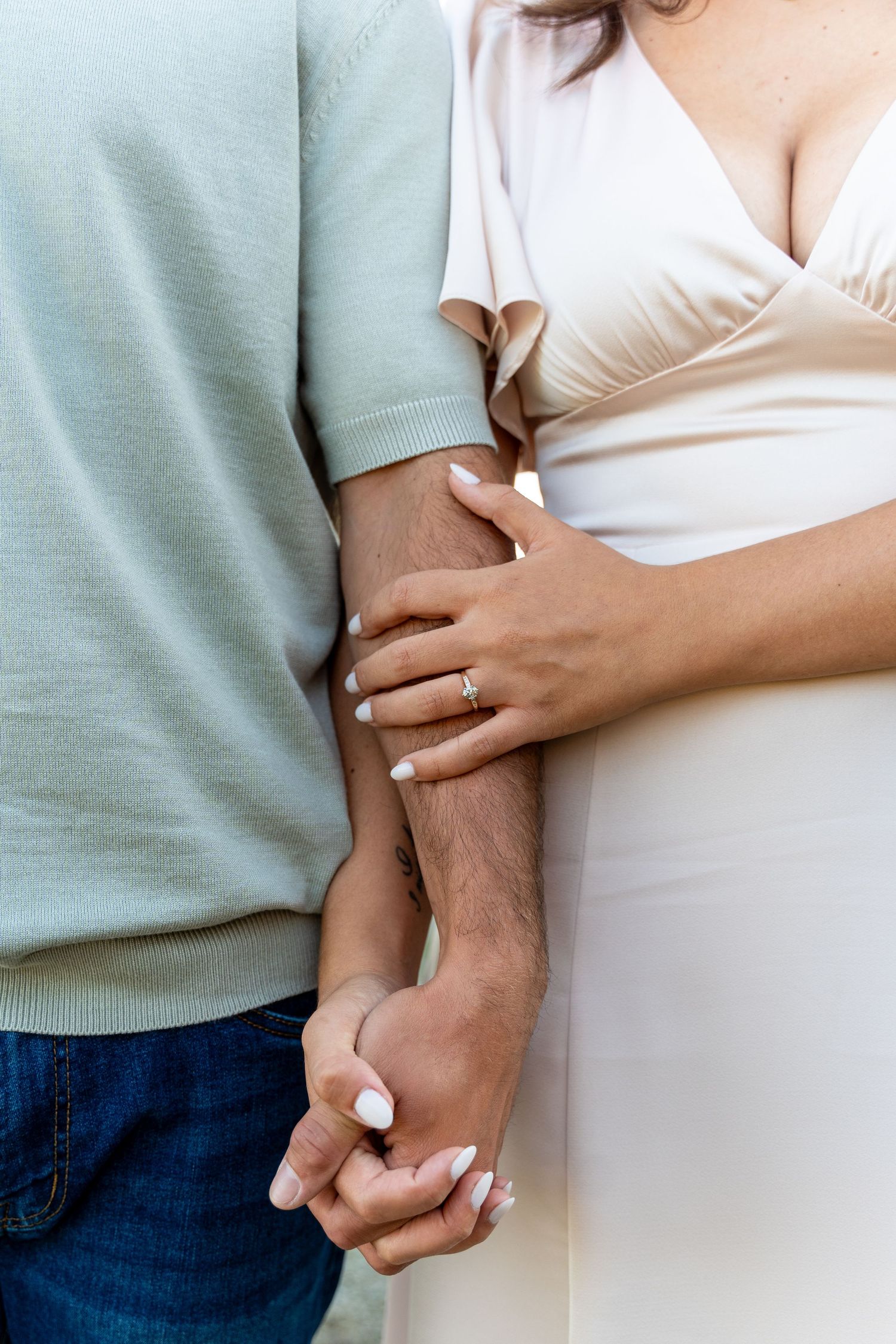 Close up of two people holding hands with white dress and mint sweater showing affection.