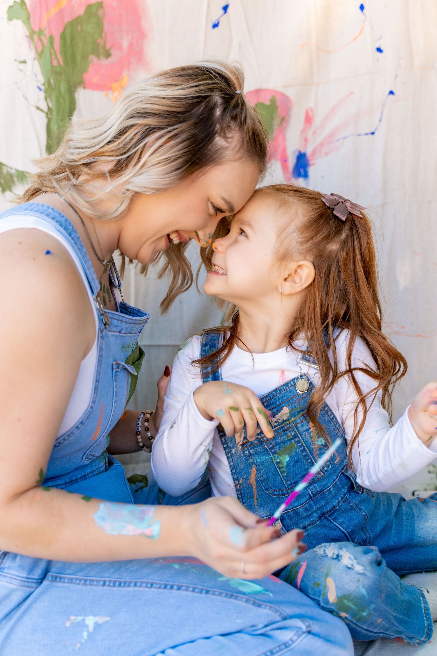 A tender bonding moment between parent and child wearing matching denim overalls while painting together.