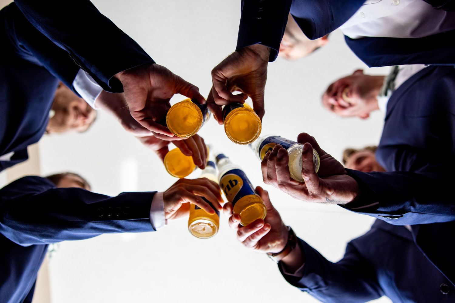Wedding party members in suits raise drinks together for celebratory toast from below angle.