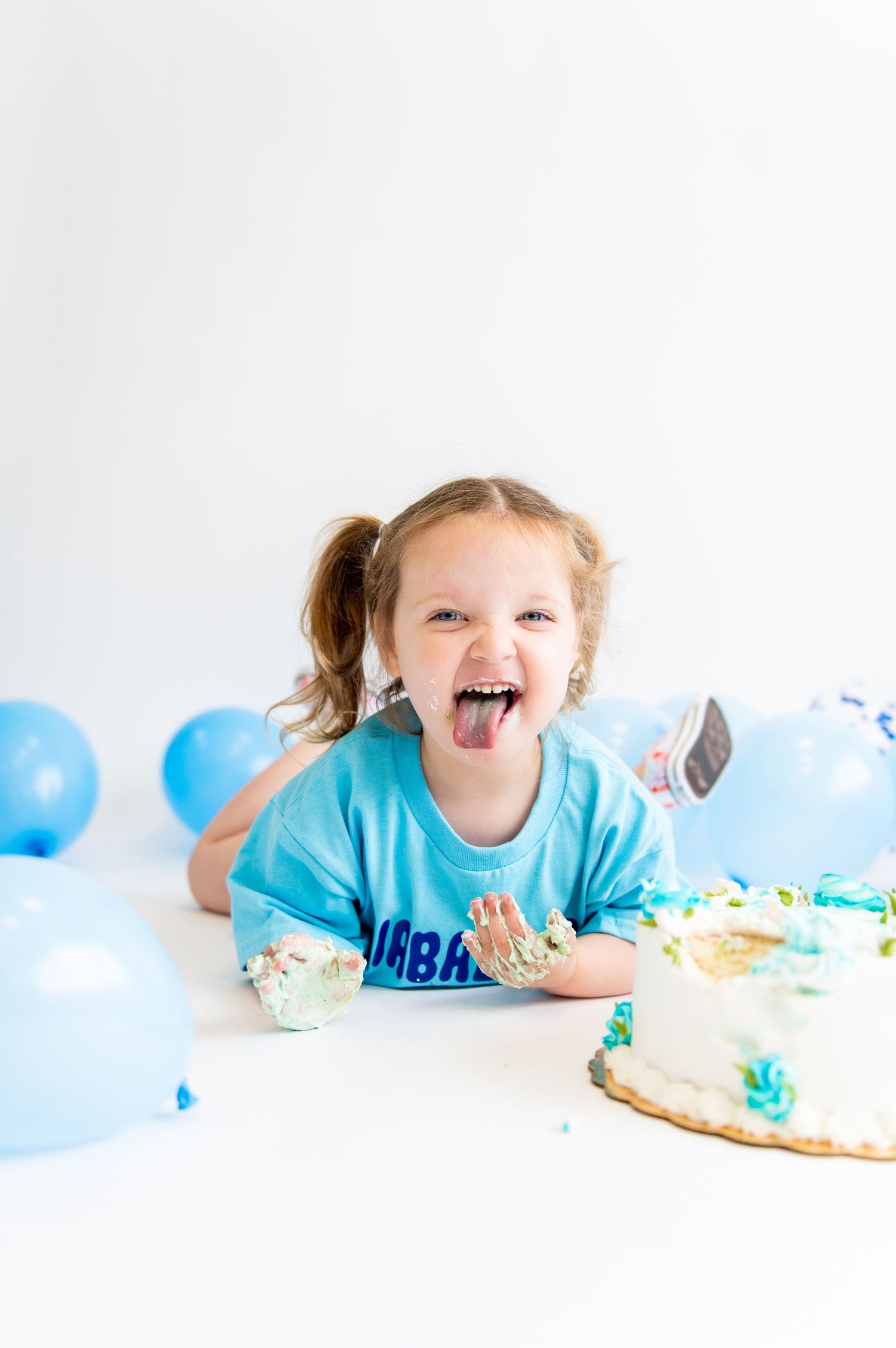 Child in blue shirt enjoying cake and balloons at birthday celebration.