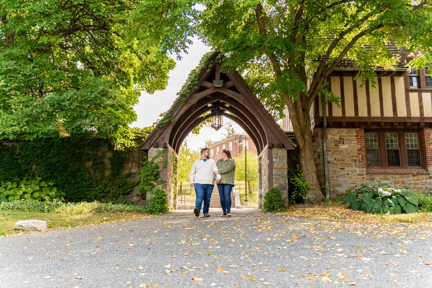 Couple standing together under Gothic stone archway surrounded by green trees.