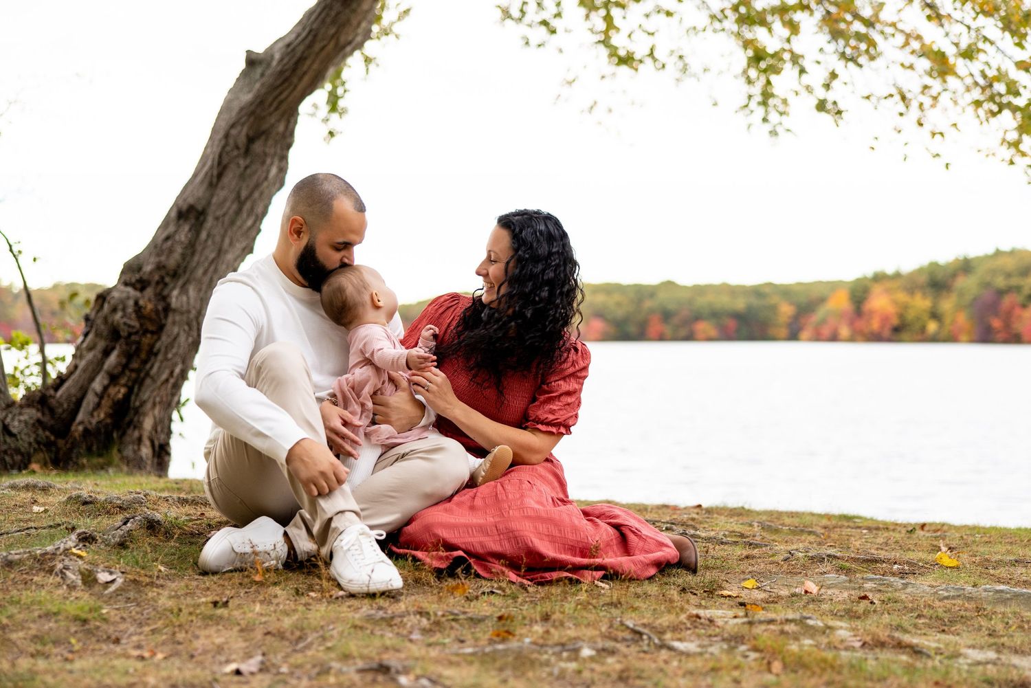 Family sits together by lakeside with fall foliage reflecting on water.