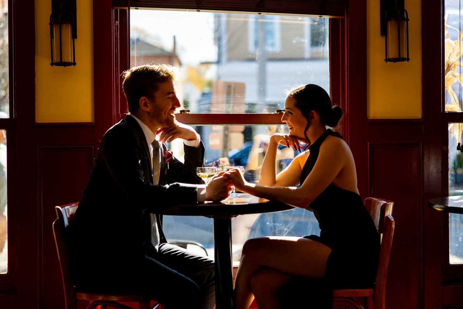 A couple enjoys drinks and conversation at a cozy bar table near a window.
