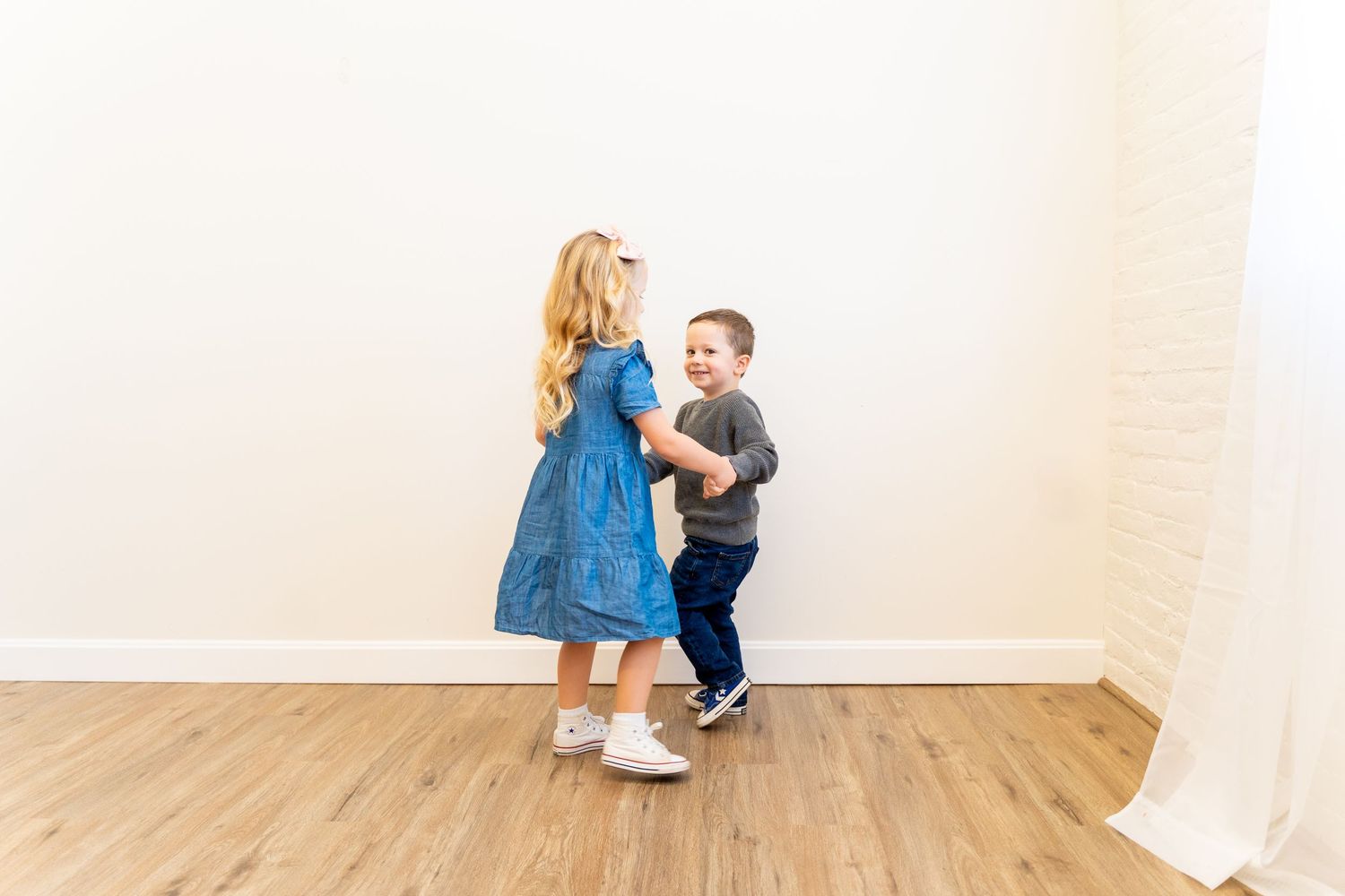 Two children in blue and gray outfits dancing together on hardwood floor.