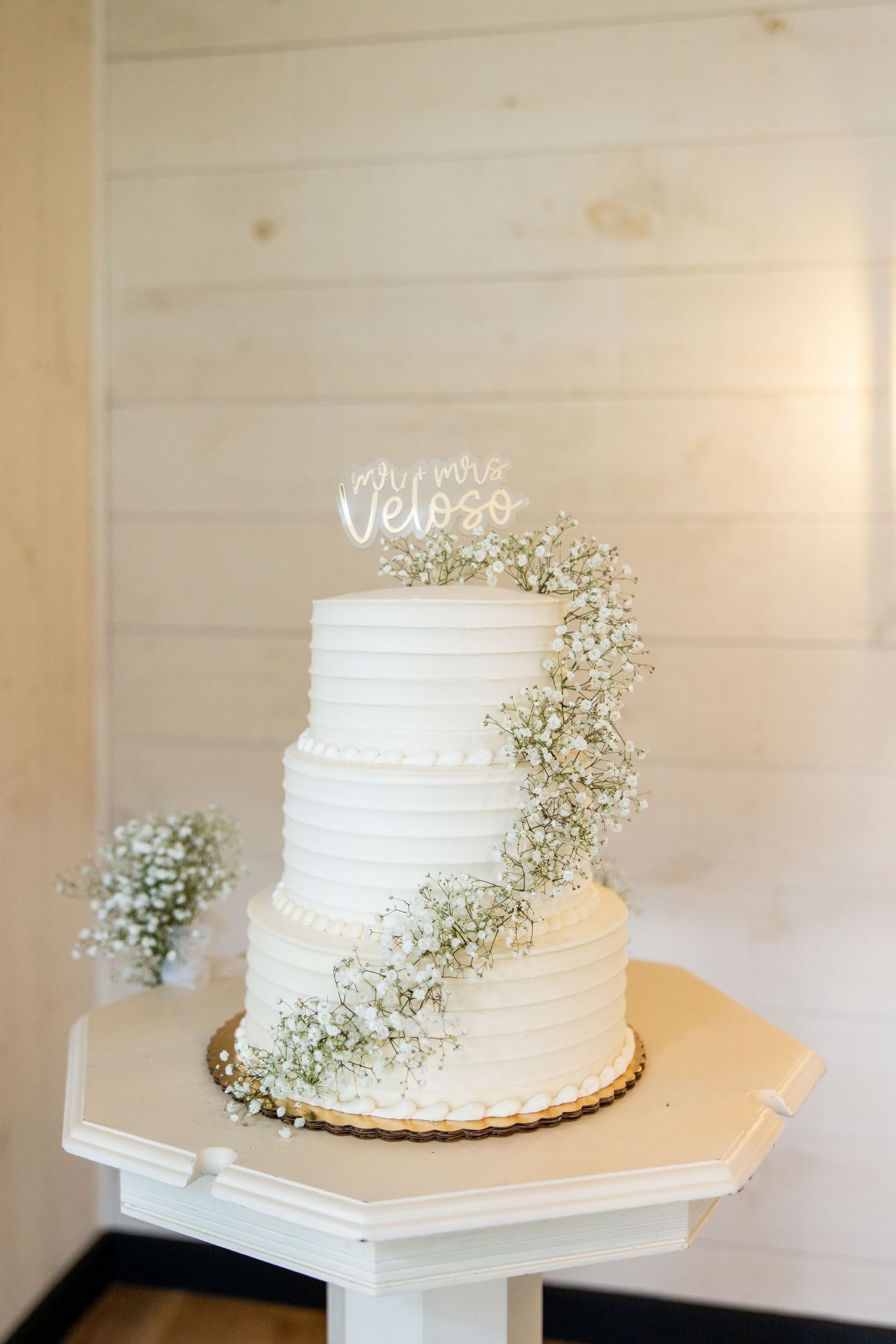 White wedding cake with textured buttercream frosting and delicate baby's breath flowers displayed on white pedestal.