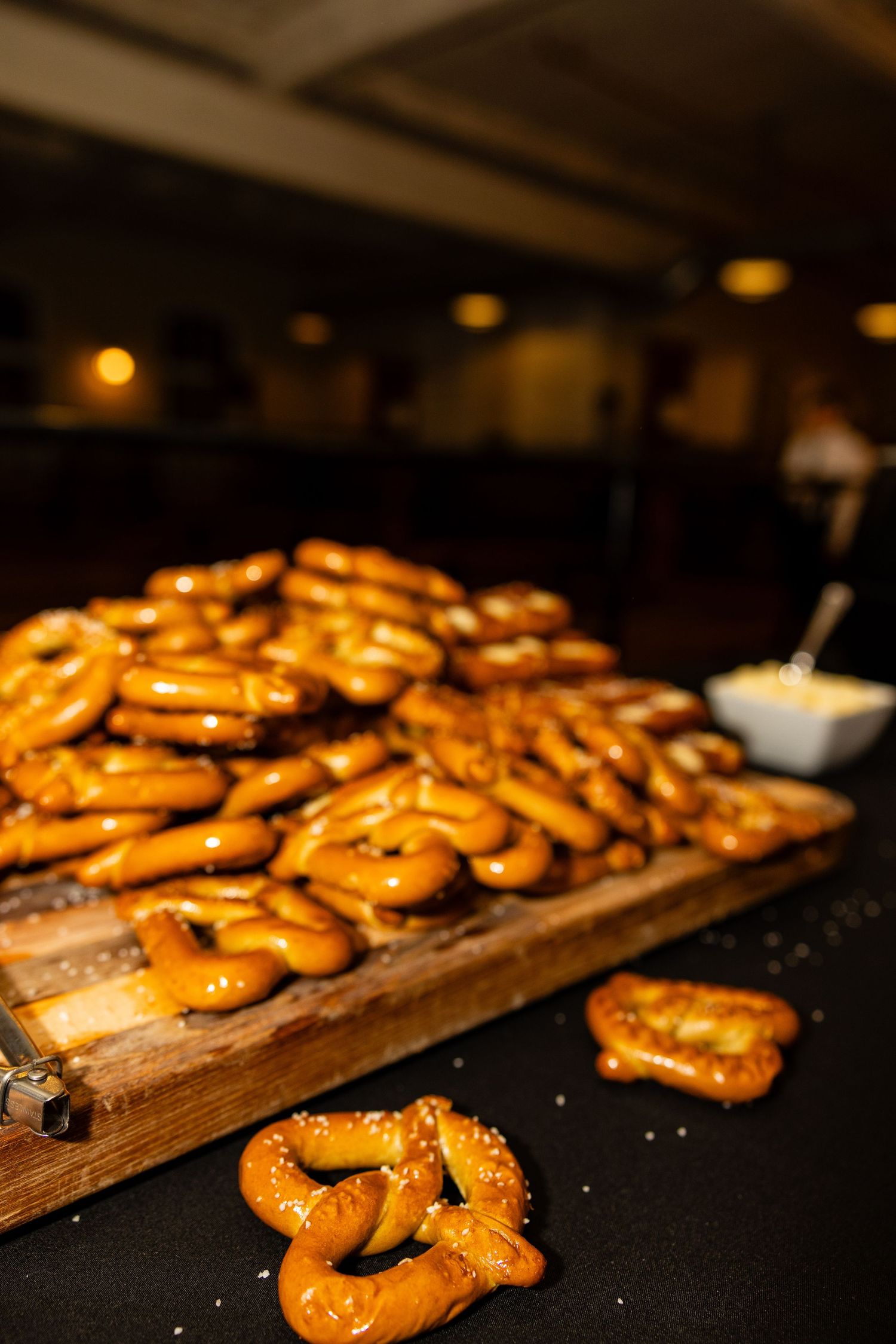 Fresh baked pretzels arranged on a wooden serving board at a social gathering.