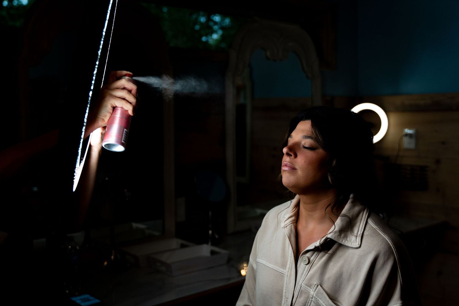 Hair stylist spraying hairspray in dramatic lighting during a beauty session.