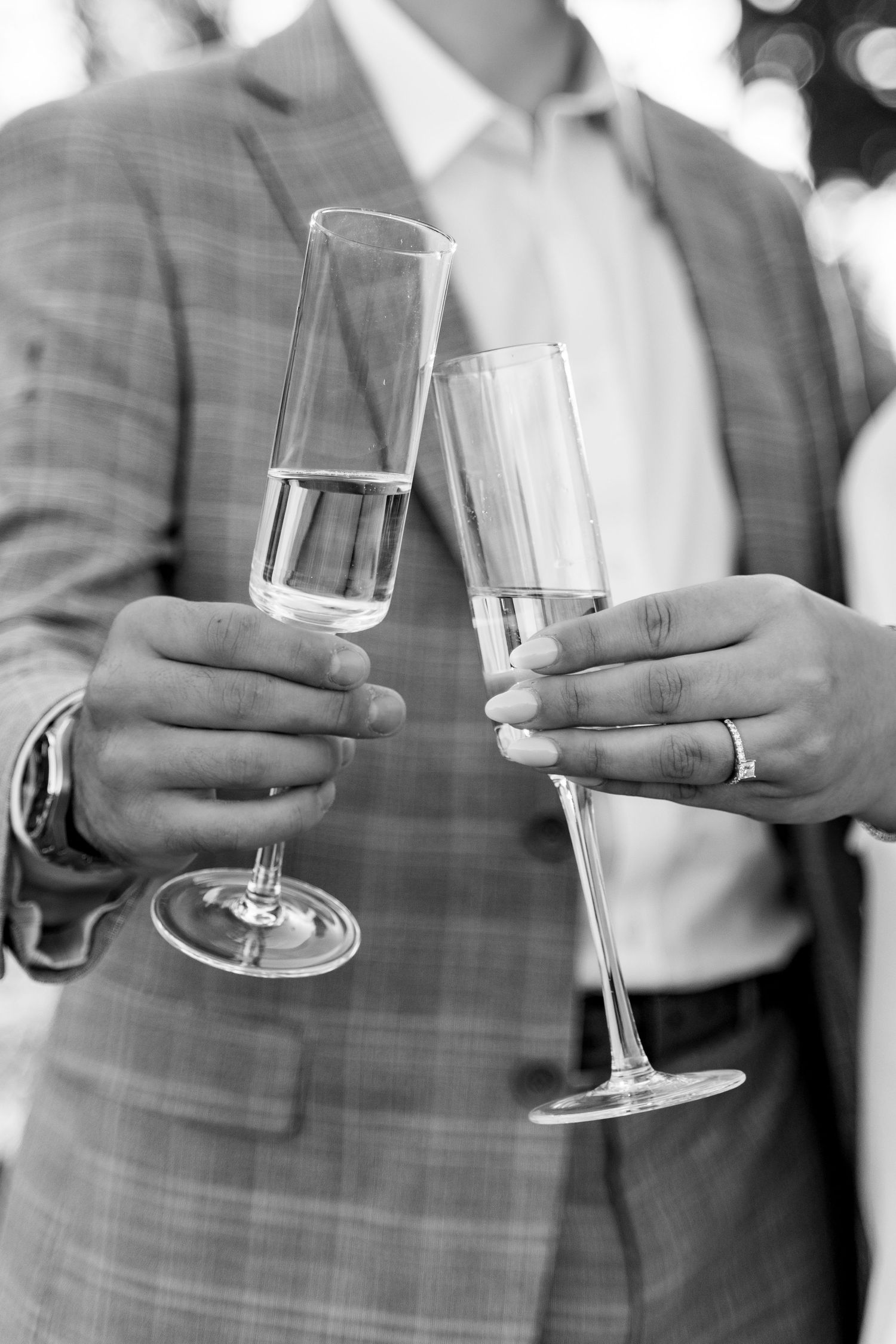 Two champagne flutes being toasted together in a black and white photo.