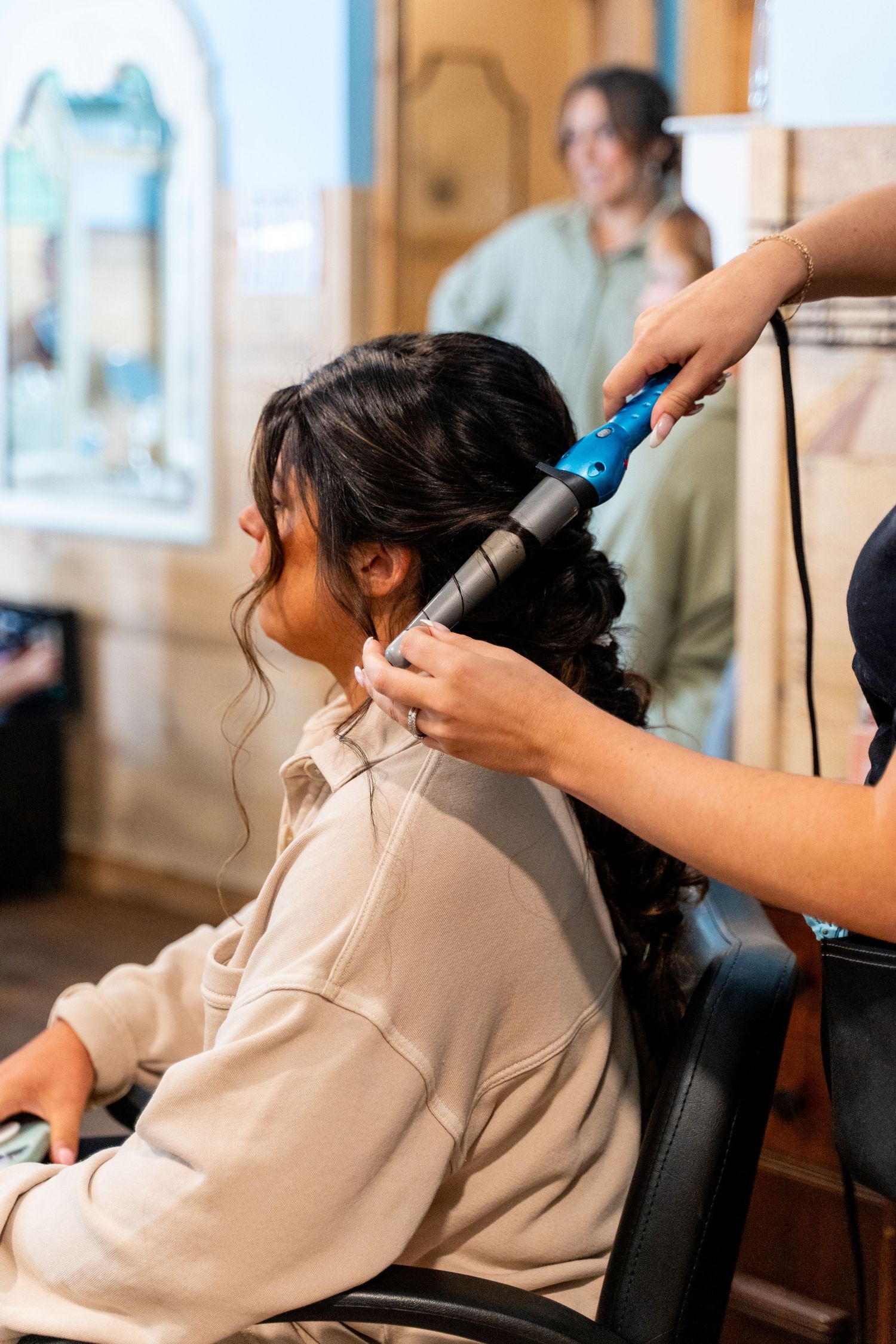 Hairstylist using a blue curling iron to style hair in a salon setting.