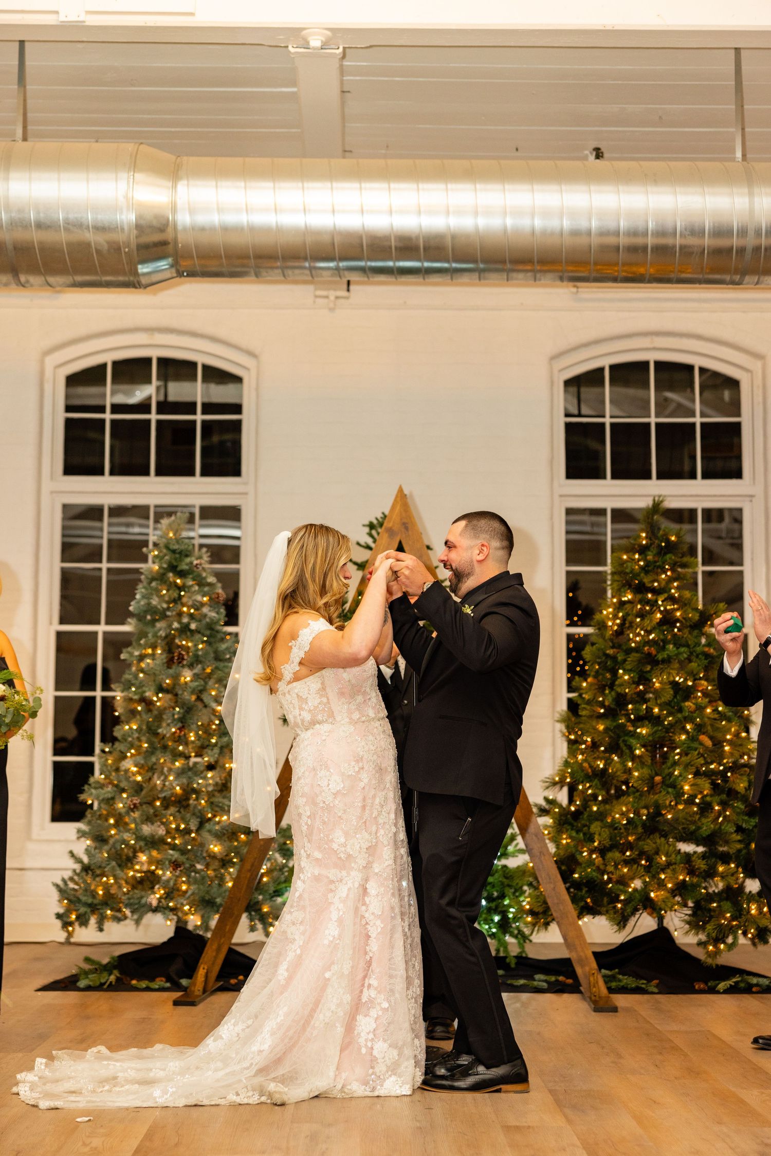 Newlyweds share a romantic moment between lit Christmas trees during their winter wedding celebration.