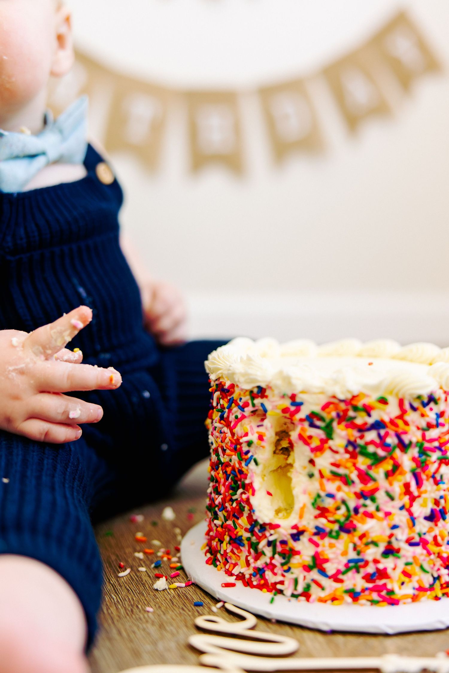 Close-up of sprinkle-covered birthday cake with small hands reaching for it.