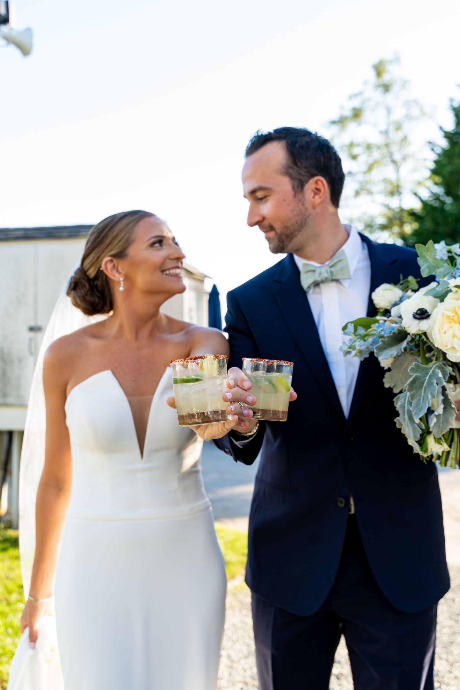 Newlyweds sharing celebratory drinks outdoors at waterfront venue.