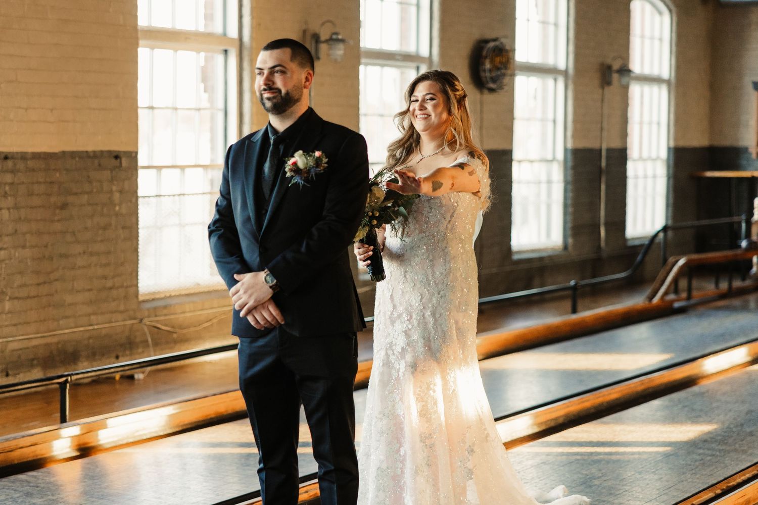 Couple poses in intimate first look moment at industrial venue with vintage bowling lanes in background.