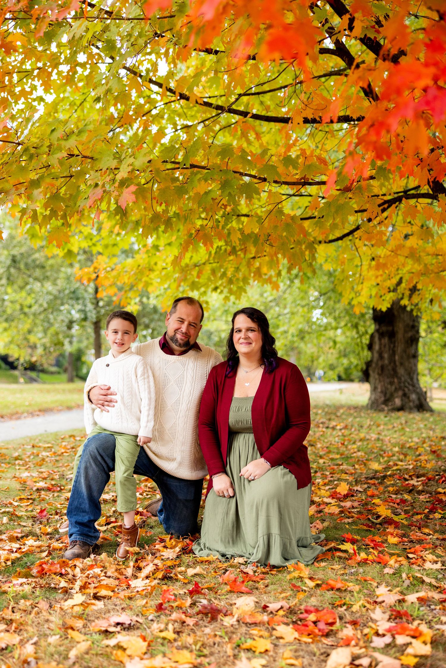 Family enjoying autumn colors under vibrant maple trees with fallen leaves in a park setting.