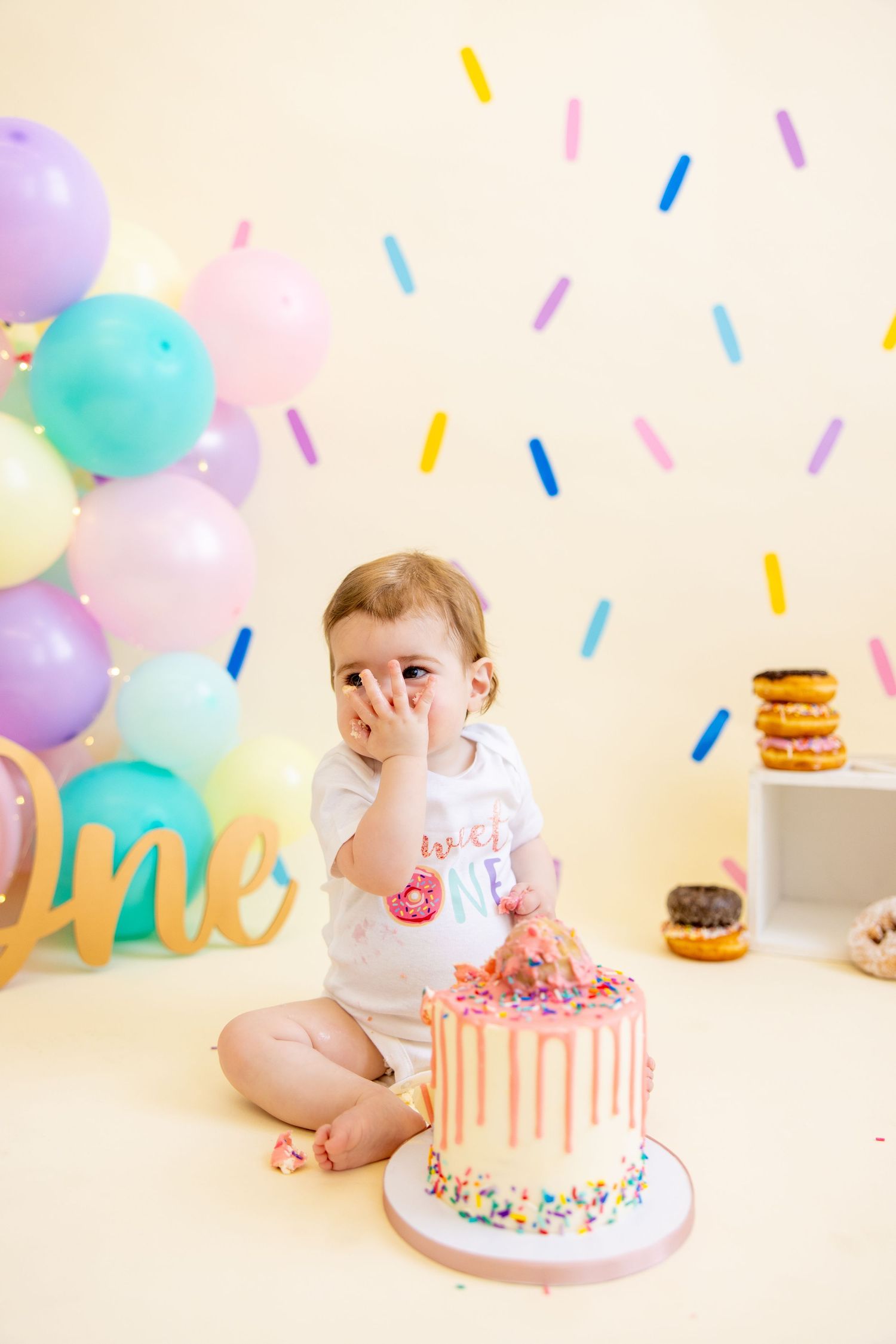 Baby with messy face giggles while celebrating first birthday with pink drip cake.