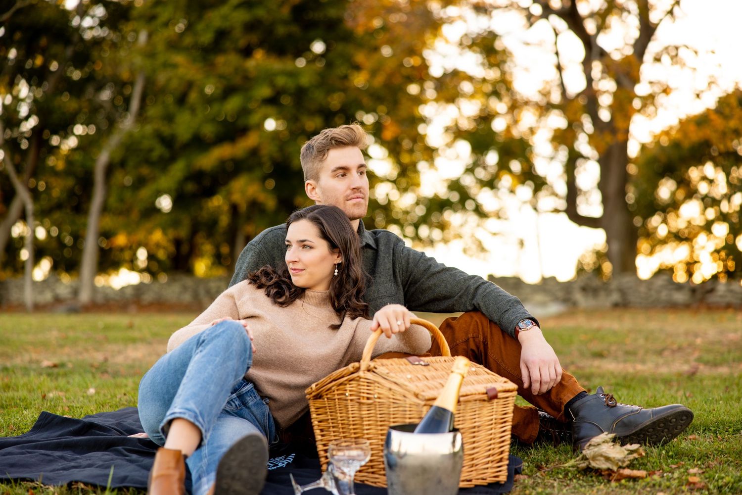 A couple enjoys a romantic picnic with a wicker basket on autumn grass.
