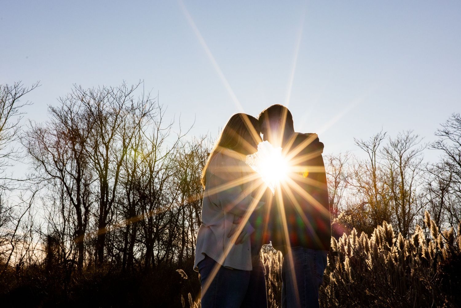 Sun bursts between couple during sunset creating dramatic starburst effect.