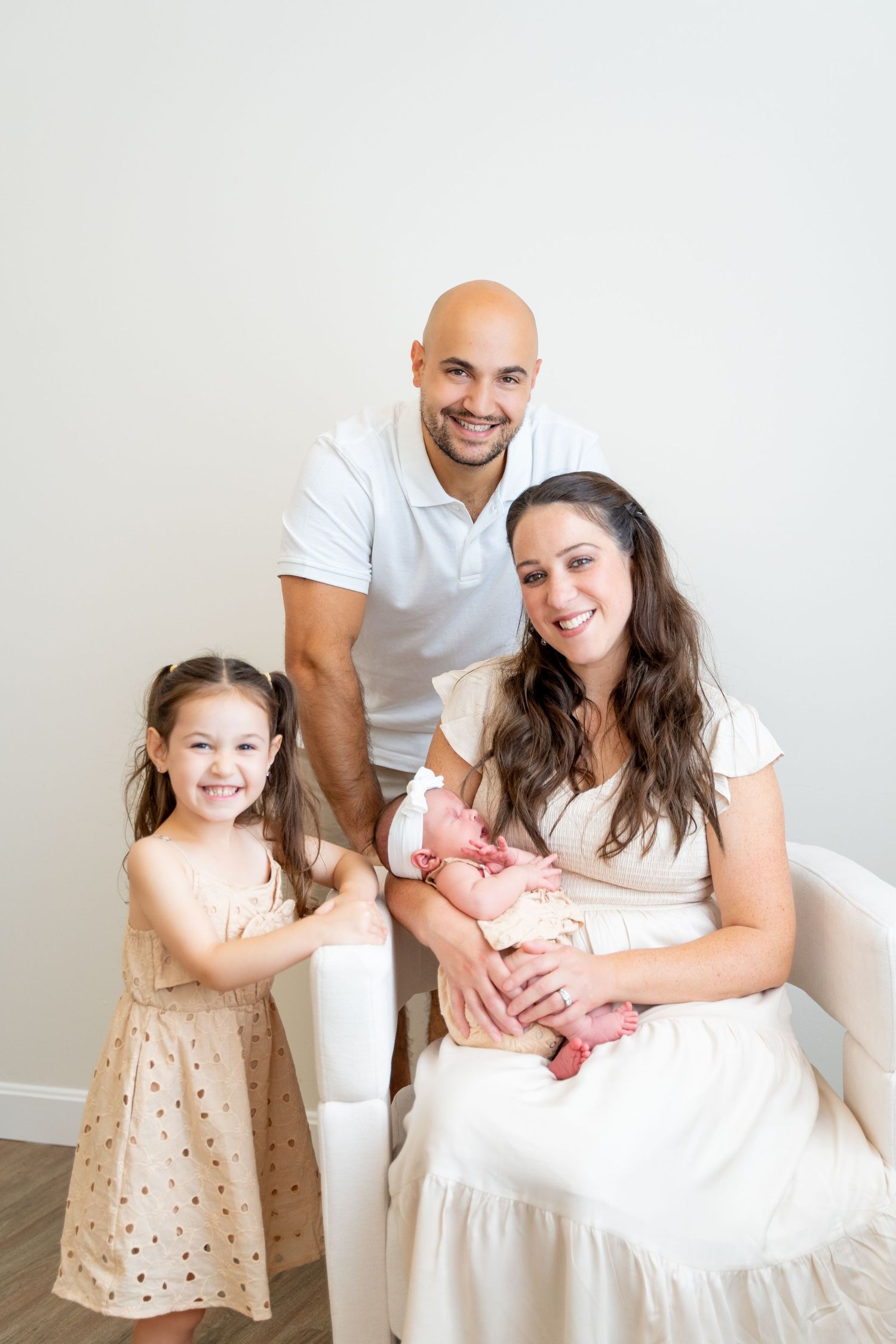 Happy family portrait with parents, young daughter and newborn in white room setting.