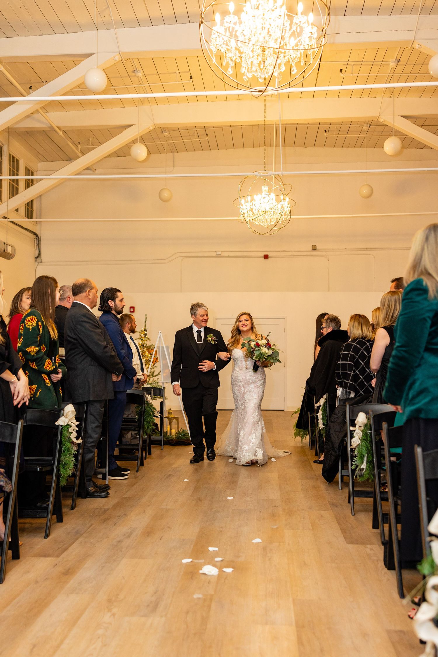 A bride walks down the aisle with her escort in a beautifully lit ceremony space.