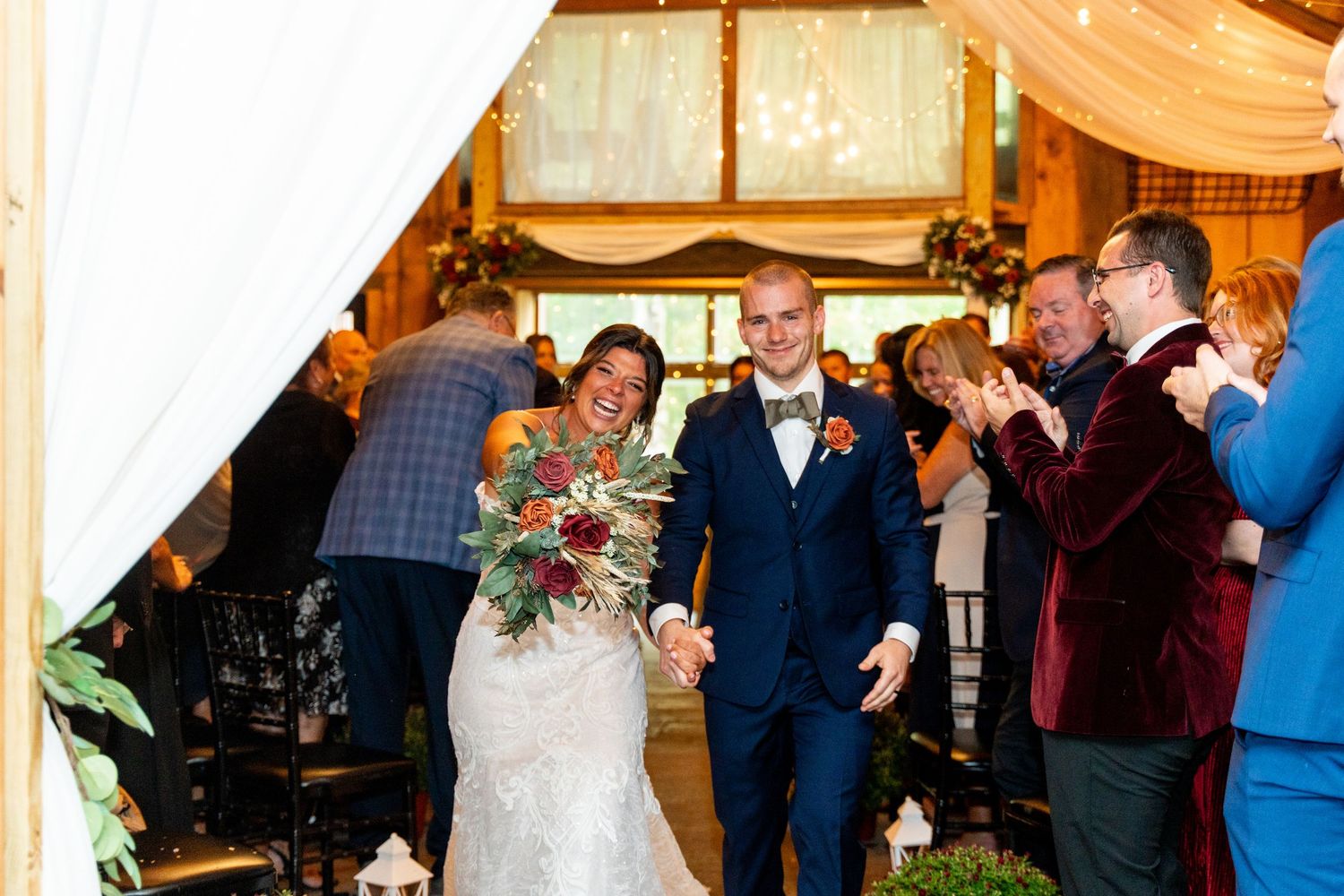 Newlyweds exit barn ceremony while guests applaud with joyful celebration.
