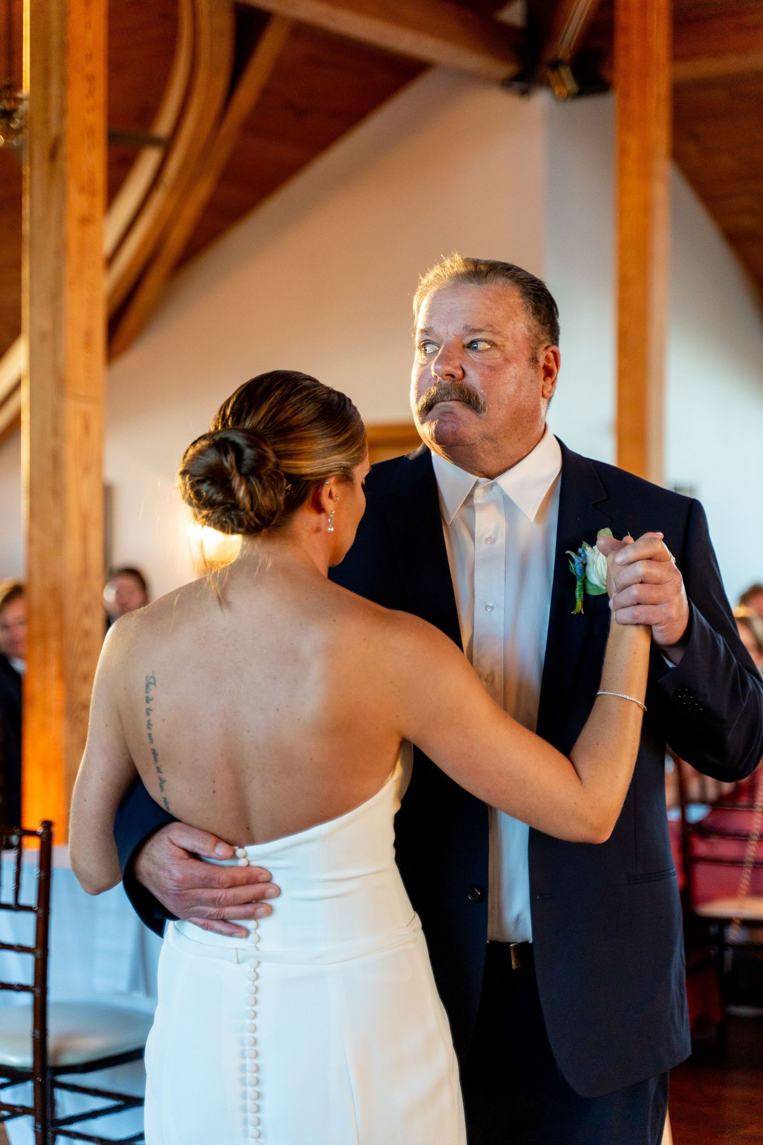 A touching father-daughter dance moment at a wedding reception in a rustic wooden venue.