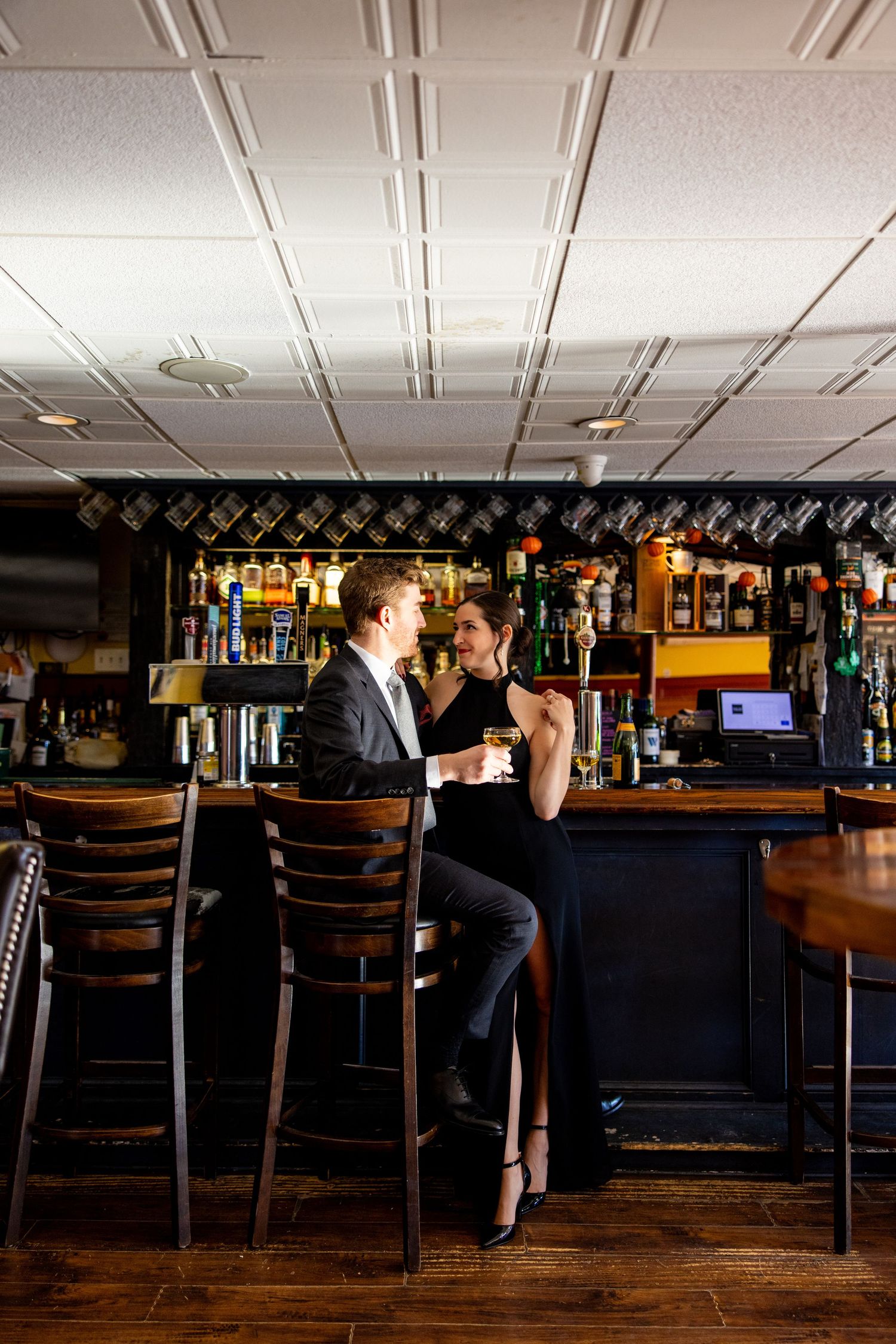 Couple shares intimate moment at dimly lit bar counter with bottles displayed behind.