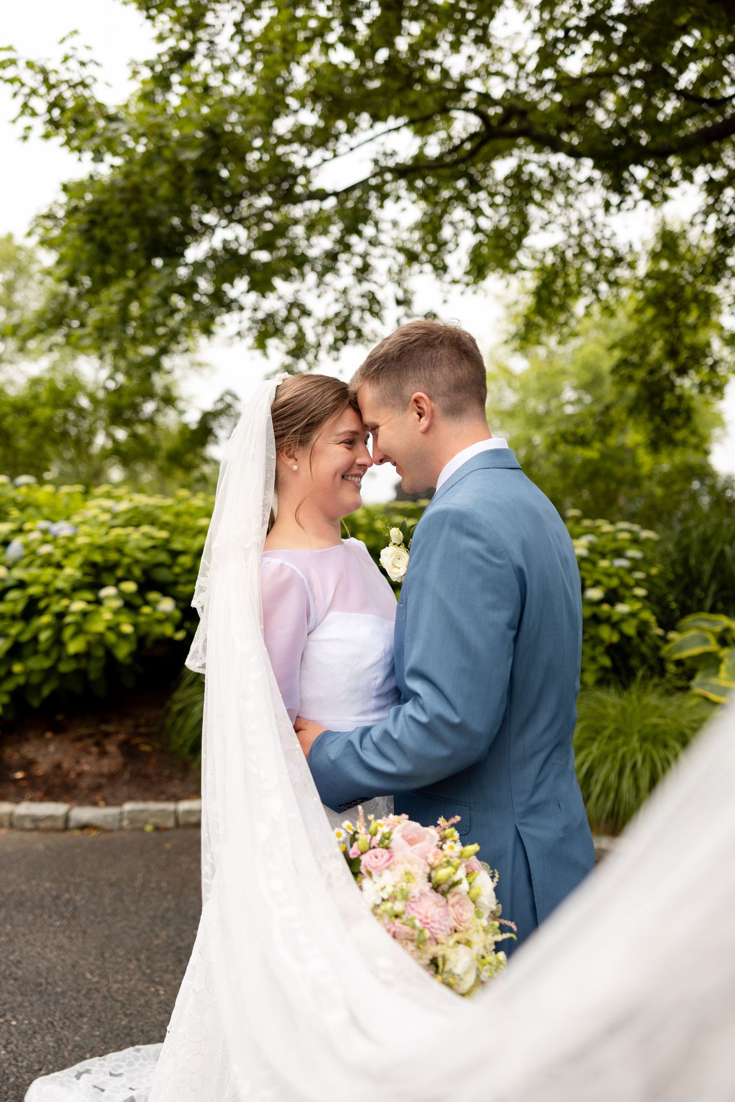 A romantic outdoor wedding moment with a couple embracing as the bride's veil flows in the breeze.