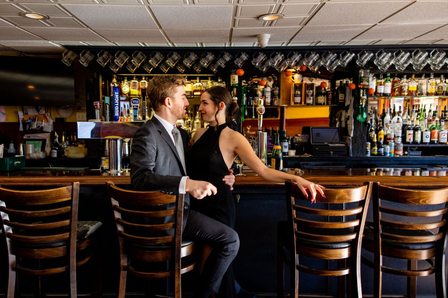 Couple in formal attire enjoys drinks while seated at modern bar counter.