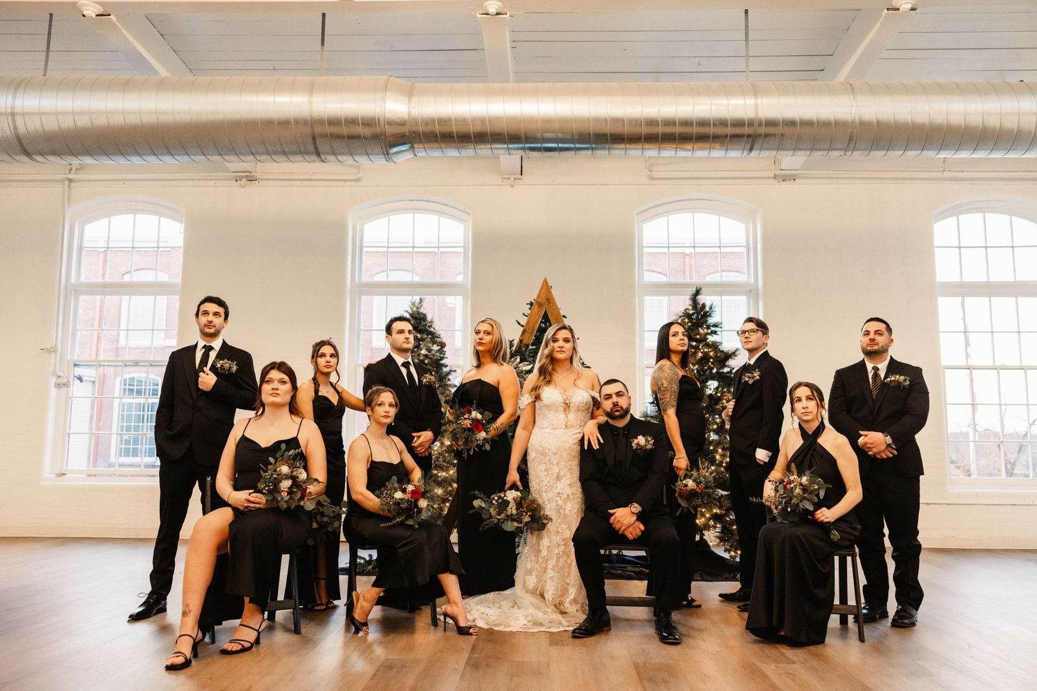 Full wedding party in formal black attire poses together in bright industrial space.
