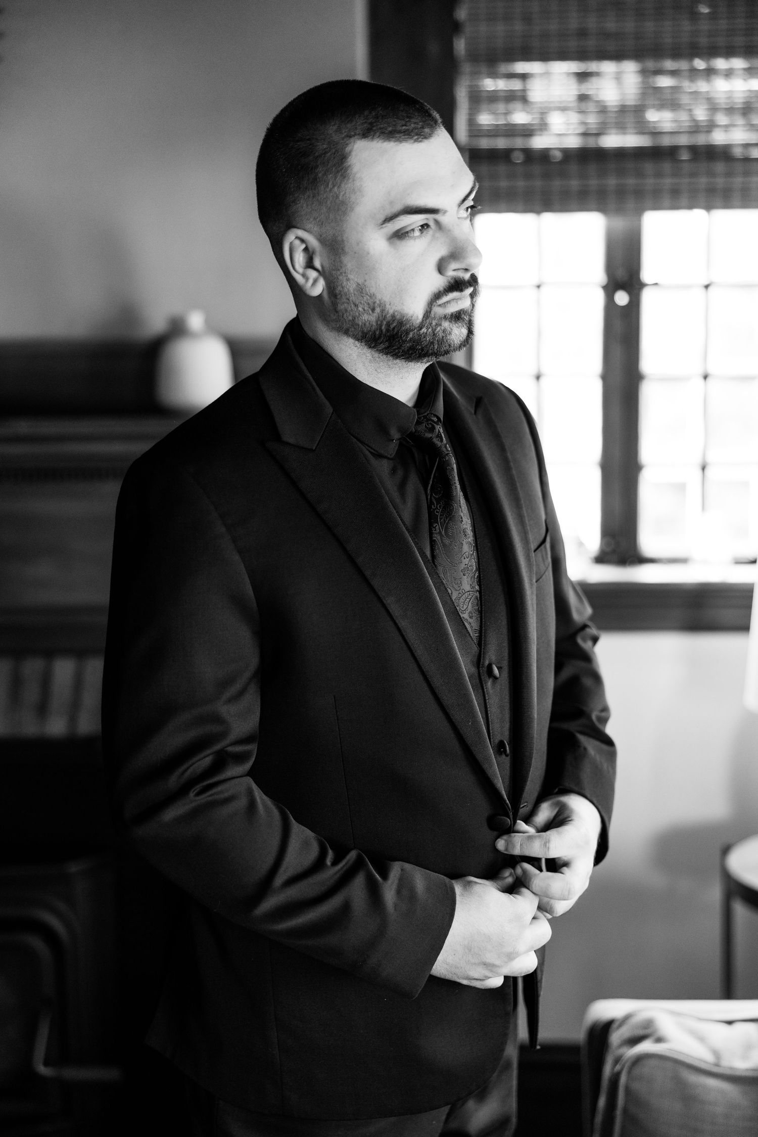 Man in black suit and tie adjusting his jacket indoors.