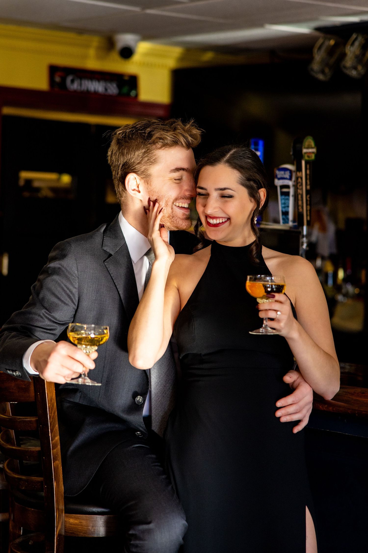 Couple enjoying drinks and laughter at pub with Guinness sign visible.