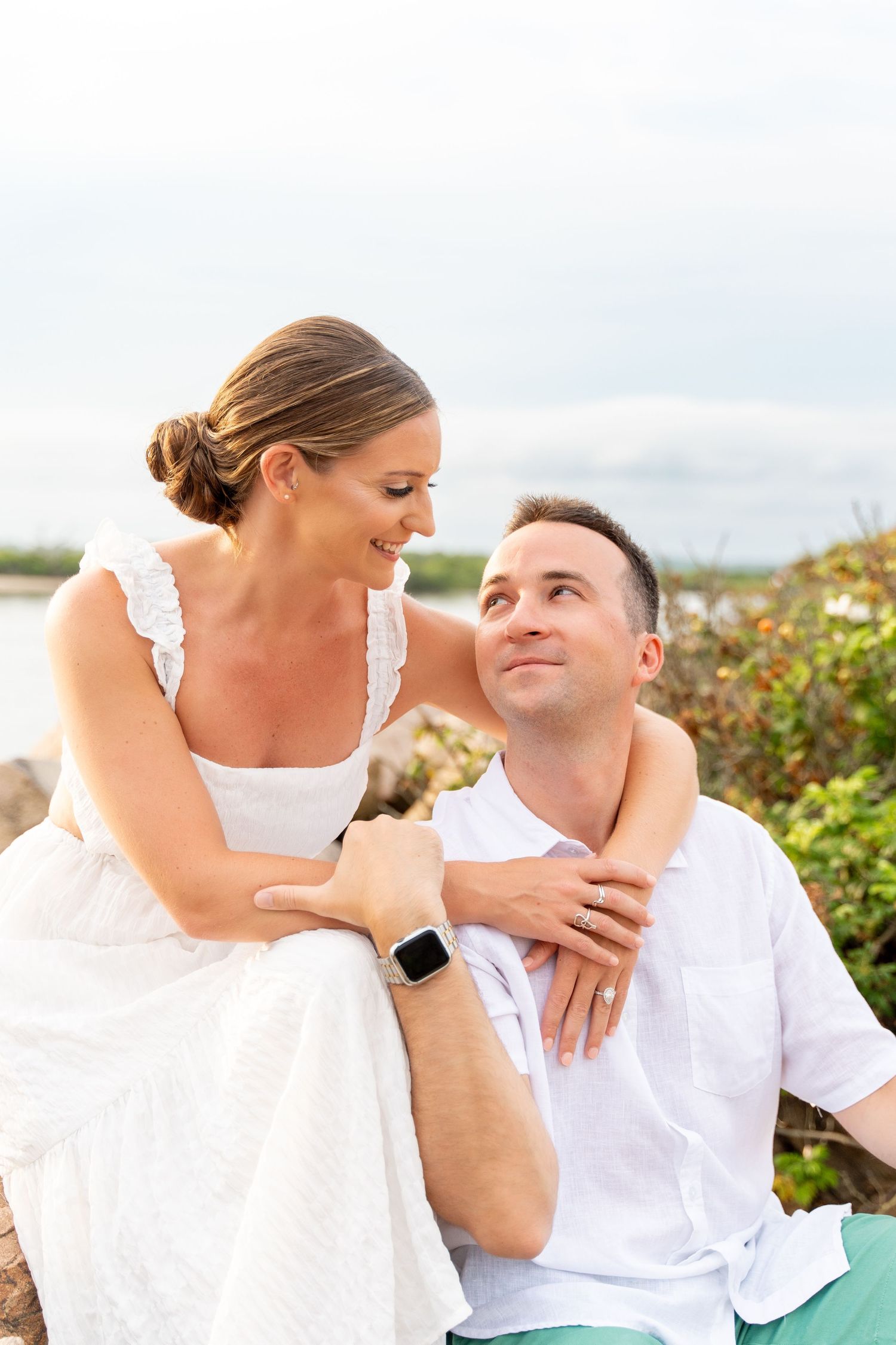 A tender moment between two people sitting on coastal rocks during a beach photoshoot.