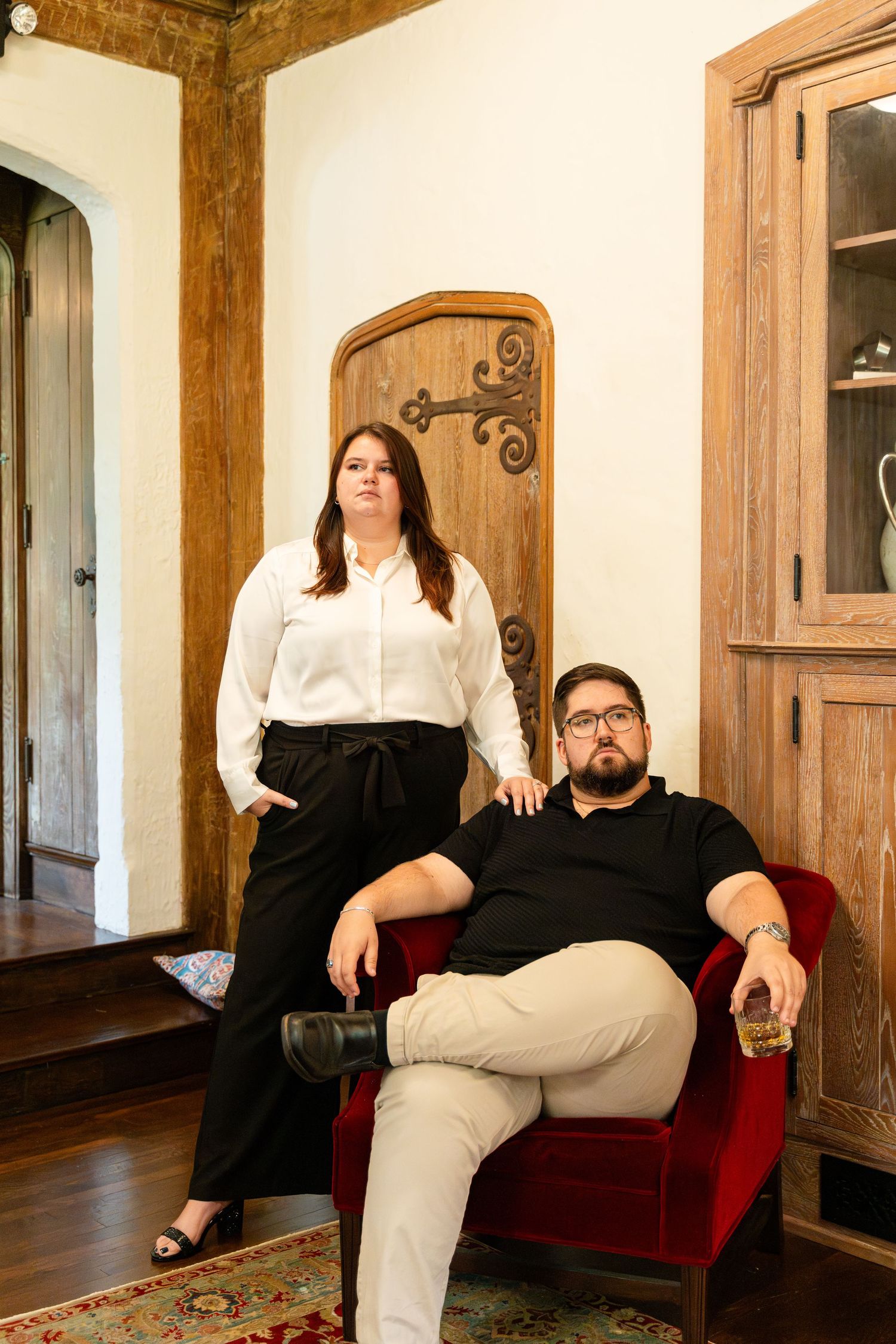 Portrait of couple sitting on red velvet chair in elegant rustic room.
