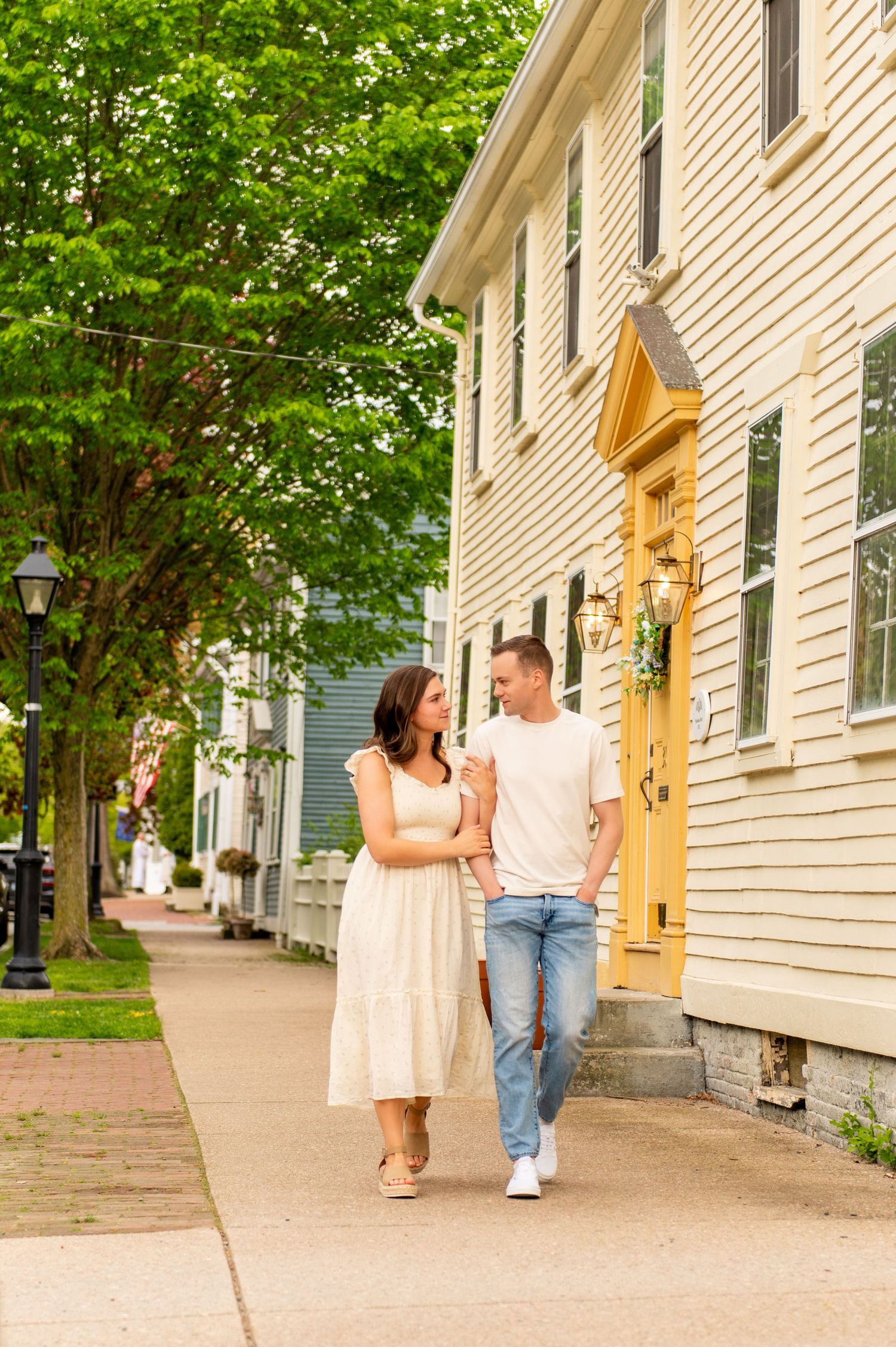 Couple walking together on sidewalk beside charming white colonial style houses.