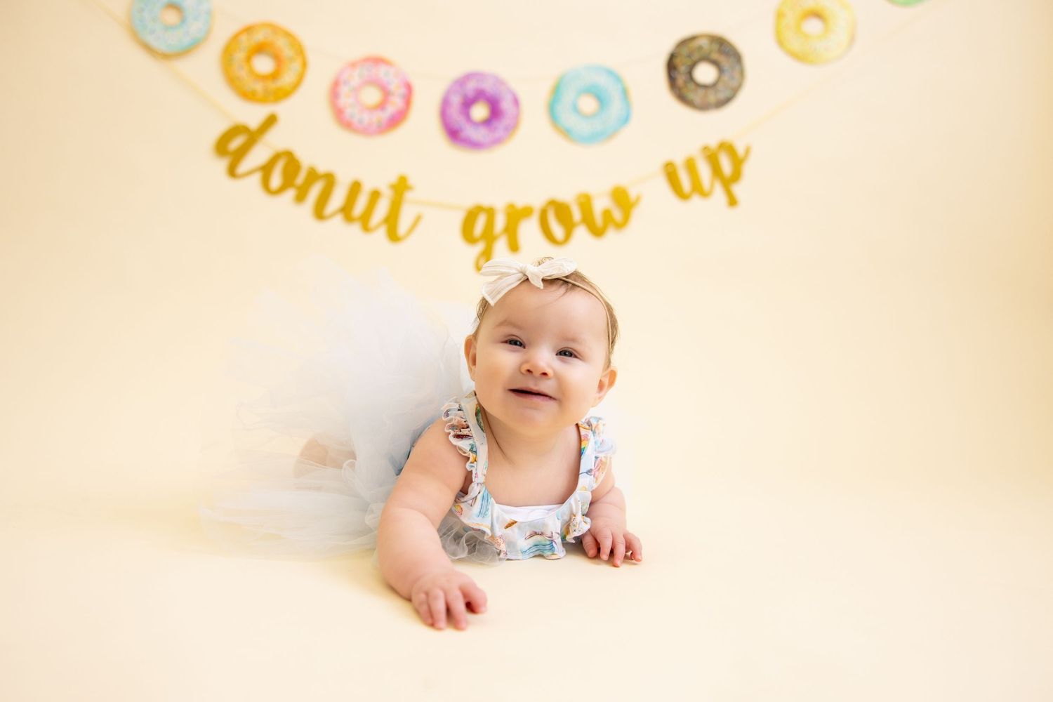 Baby in tulle outfit poses under donut-themed party banner.