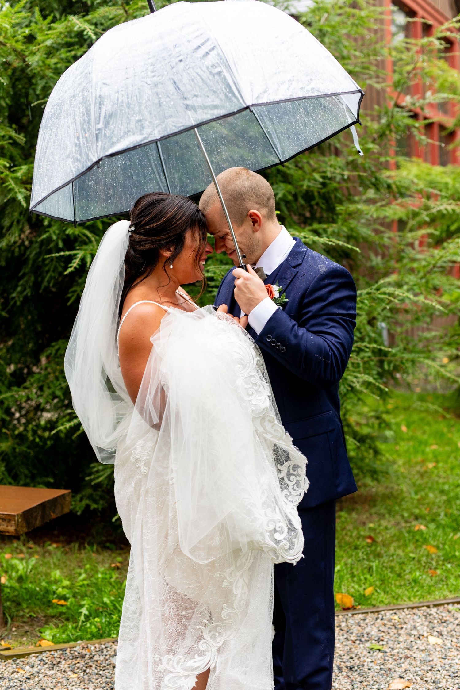 A couple shares an intimate moment under a clear umbrella during their rainy wedding day.